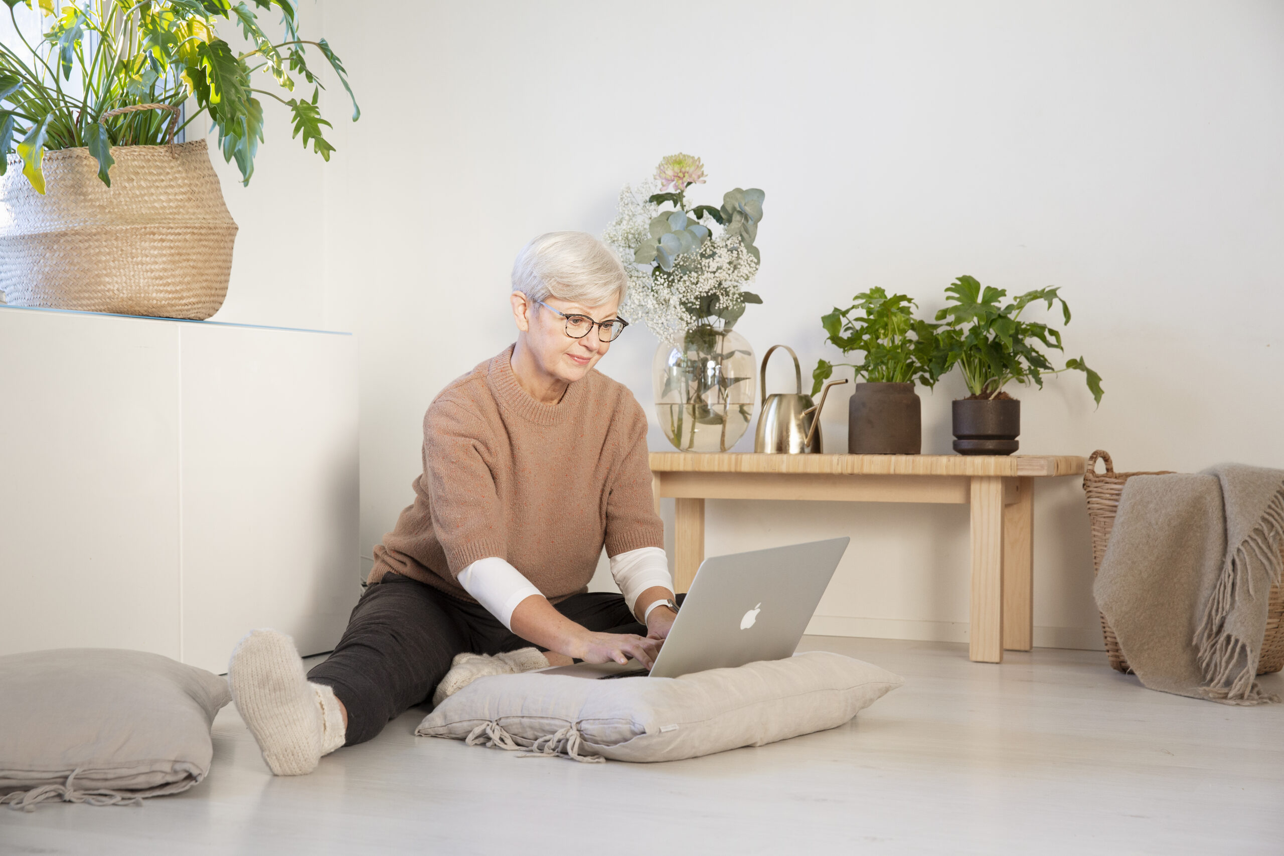 Nainen istuu rennosti lattialla ja näppäilee tietokonetta.